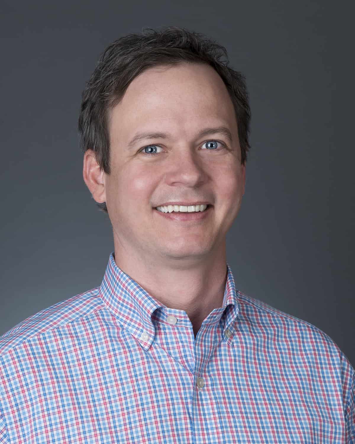 Professional portrait of a mortgage lending expert at GMFS Partners, smiling and dressed in a checkered shirt, representing trusted mortgage services and financial expertise.