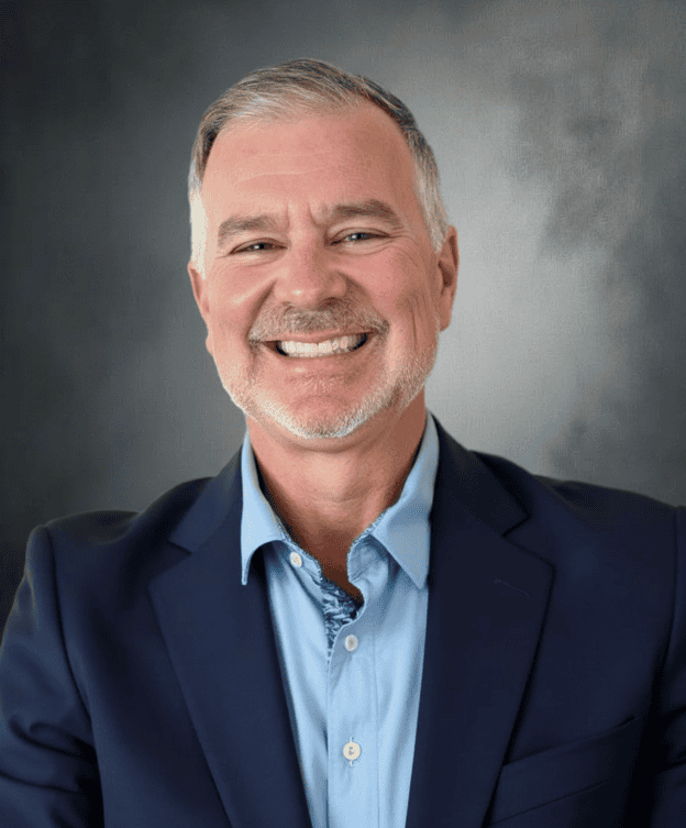 Smiling middle-aged man in a navy suit and light blue shirt, professional portrait for GMFS Partners.