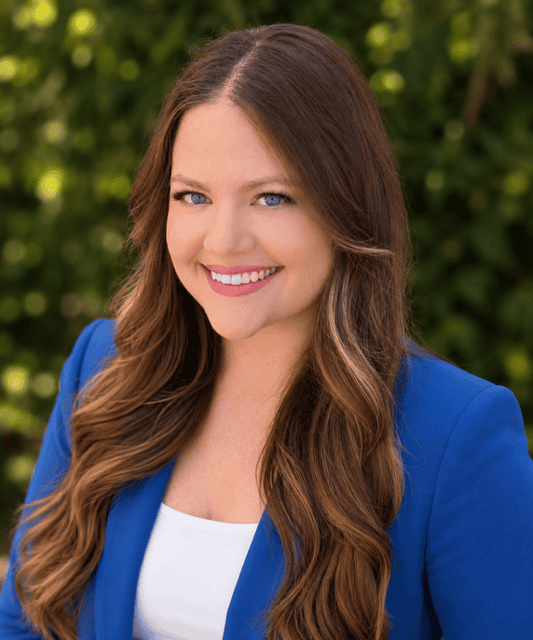Professional portrait of Rebecca Collins, smiling woman with long brown hair in a blue blazer, outdoors with greenery background.